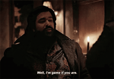 A Man With A Beard Is Standing In A Dark Room And Talking To Another Man . GIF