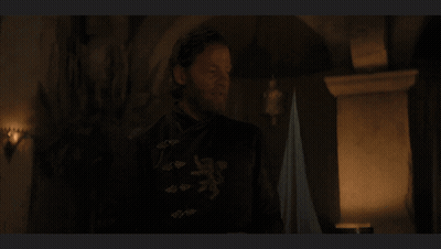 A Man With A Beard Is Standing In A Dark Room In Front Of A Fireplace GIF