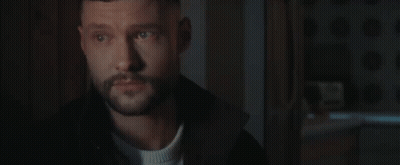 A Man With A Beard Is Standing In A Dark Room Looking At Something . GIF