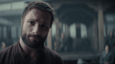 A Man With A Beard Is Standing In A Dark Room Looking At The Camera . GIF