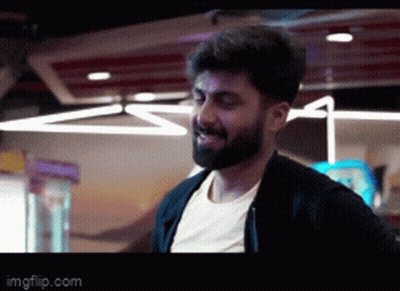 A Man With A Beard Is Standing In A Dark Room . GIF