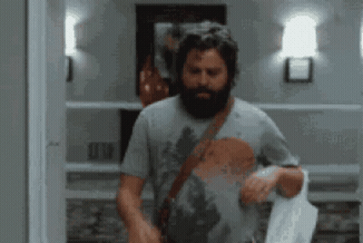 A Man With A Beard Is Standing In A Hallway Holding A Towel GIF