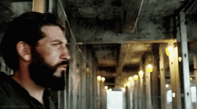 A Man With A Beard Is Standing In A Hallway Looking Out The Window . GIF