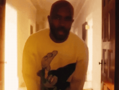 A Man With A Beard Is Standing In A Hallway Wearing A Yellow Sweater . GIF