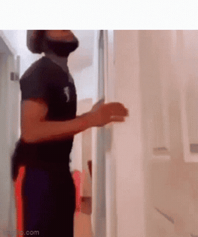 A Man With A Beard Is Standing In A Hallway With His Hands Up . GIF