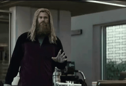 A Man With A Beard Is Standing In A Room In Front Of A Window . GIF