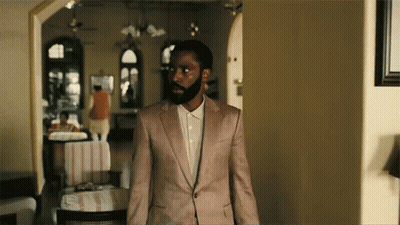 A Man With A Beard Is Standing In A Room Wearing A Pink Suit And White Shirt . GIF