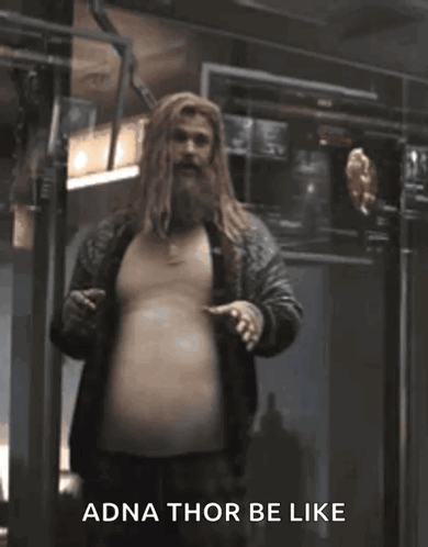 A Man With A Beard Is Standing In A Room With The Words Adna Thor Be Like Written On The Bottom . GIF