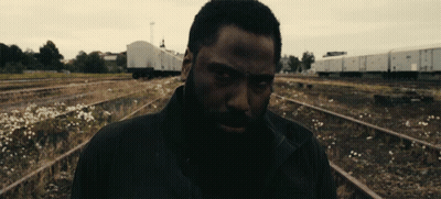 A Man With A Beard Is Standing In A Train Yard GIF