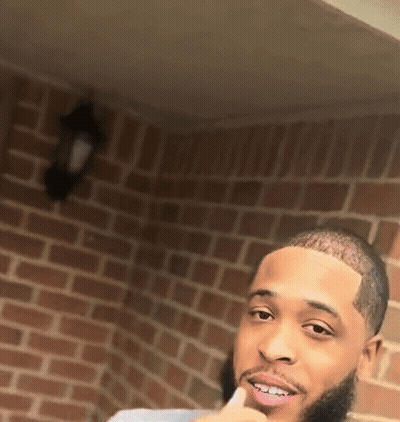 A Man With A Beard Is Standing In Front Of A Brick Wall . GIF