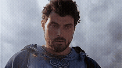 A Man With A Beard Is Standing In Front Of A Cloudy Sky And Looking At The Camera . GIF