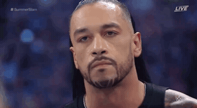 A Man With A Beard Is Standing In Front Of A Crowd And Looking At The Camera . GIF