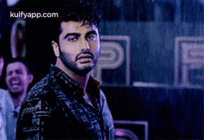 A Man With A Beard Is Standing In Front Of A Crowd Of People In A Dark Room . GIF