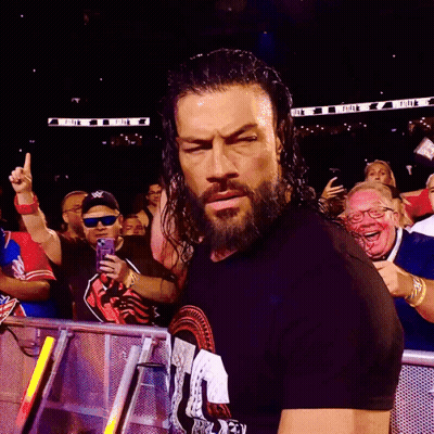 A Man With A Beard Is Standing In Front Of A Crowd With A Sign In The Background That Says ' Wwe ' GIF