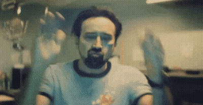 A Man With A Beard Is Standing In Front Of A Glass Door With His Hands Behind It . GIF