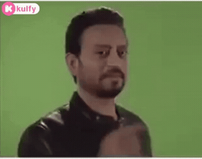 A Man With A Beard Is Standing In Front Of A Green Screen And Looking At The Camera . GIF