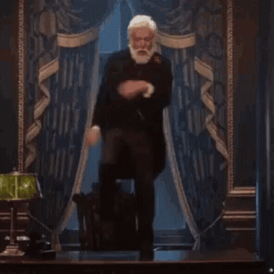 A Man With A Beard Is Standing In Front Of A Lamp In A Room . GIF