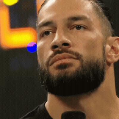 A Man With A Beard Is Standing In Front Of A Microphone And Looking At The Camera . GIF