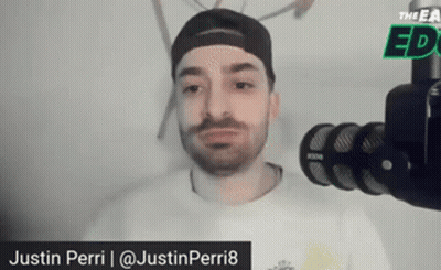 A Man With A Beard Is Standing In Front Of A Microphone And Talking Into It . GIF