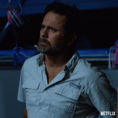 A Man With A Beard Is Standing In Front Of A Netflix Sign GIF