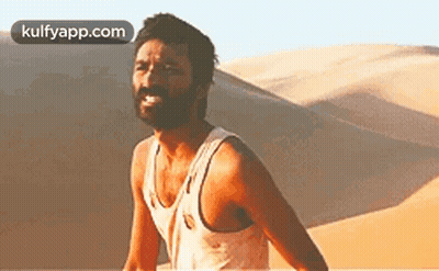 A Man With A Beard Is Standing In Front Of A Sand Dune In The Desert . GIF