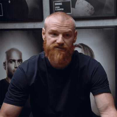A Man With A Beard Is Standing In Front Of A Sign That Says ' Gnarmac ' On It GIF