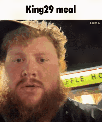 A Man With A Beard Is Standing In Front Of A Sign That Says King 29 Meal GIF