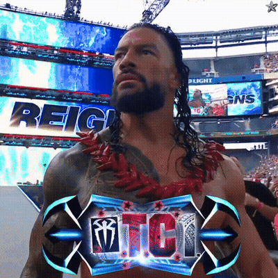 A Man With A Beard Is Standing In Front Of A Sign That Says Reigns GIF