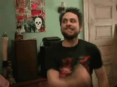 A Man With A Beard Is Standing In Front Of A Skull Poster On The Wall GIF