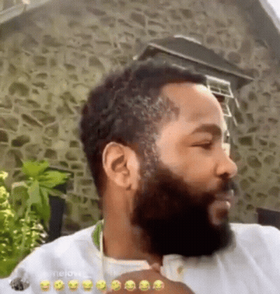 A Man With A Beard Is Standing In Front Of A Stone Building And Making A Funny Face . GIF