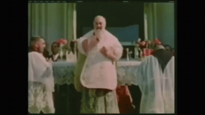 A Man With A Beard Is Standing In Front Of A Table With Flowers On It GIF