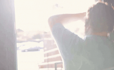 A Man With A Beard Is Standing In Front Of A Wall And Covering His Face With His Hand GIF