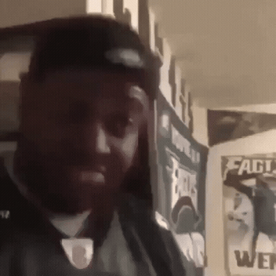 A Man With A Beard Is Standing In Front Of A Wall With A Banner That Says Eagles On It . GIF