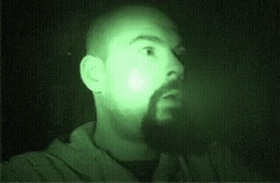 A Man With A Beard Is Standing In The Dark With A Green Light Shining On His Face . GIF