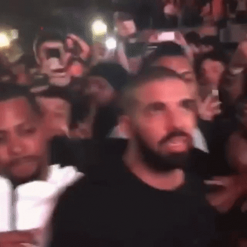 A Man With A Beard Is Standing In The Middle Of A Crowd Of People . GIF
