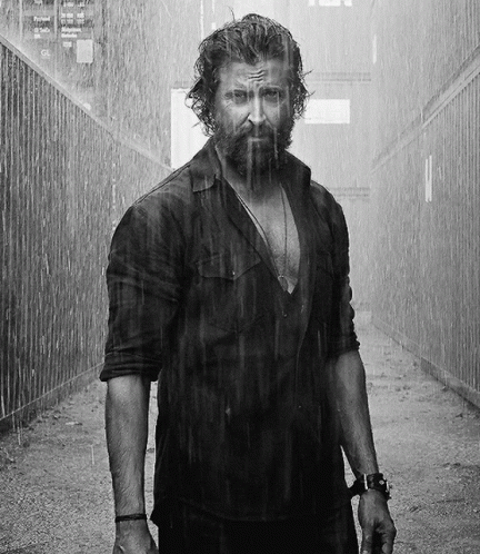 A Man With A Beard Is Standing In The Rain Looking At The Camera GIF