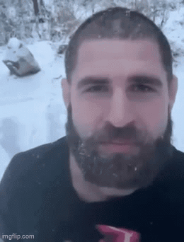 A Man With A Beard Is Standing In The Snow GIF
