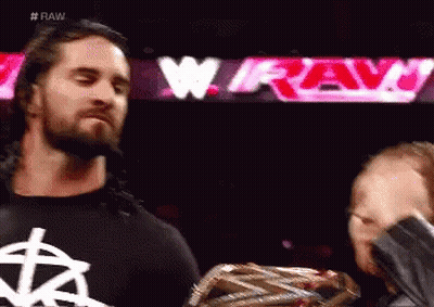 A Man With A Beard Is Standing Next To Another Man Holding A Wrestling Championship Belt . GIF
