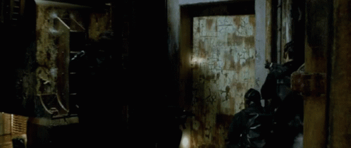 A Man With A Beard Is Standing Next To Another Man In A Dark Room . GIF