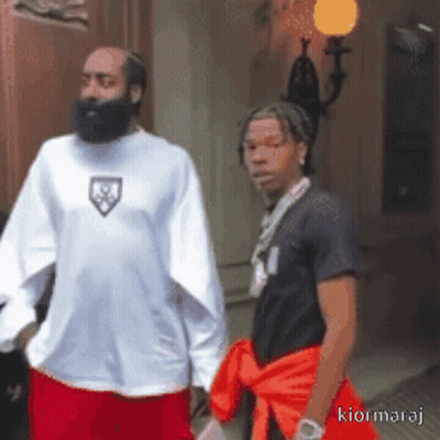 A Man With A Beard Is Standing Next To Another Man With A Necklace Around His Neck GIF