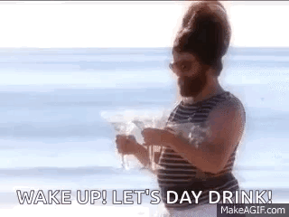 A Man With A Beard Is Standing On A Beach Holding A Drink . GIF