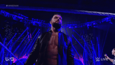 A Man With A Beard Is Standing On A Stage In Front Of A Crowd While Wearing A Black Jacket . GIF