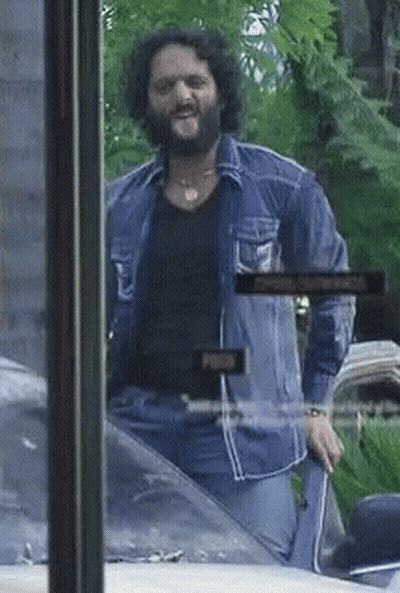 A Man With A Beard Is Sticking His Tongue Out In Front Of A Sign That Says Open GIF