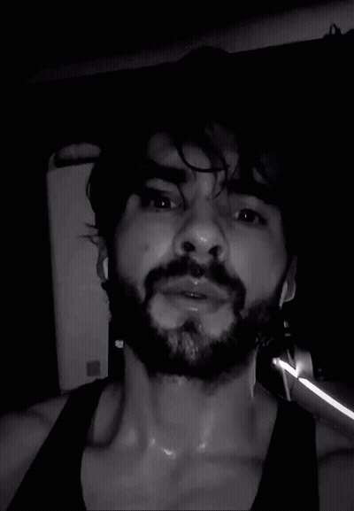A Man With A Beard Is Sweating In A Black Tank Top . GIF