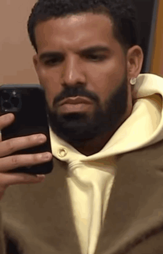 A Man With A Beard Is Taking A Picture Of Himself In A Mirror With His Cell Phone . GIF