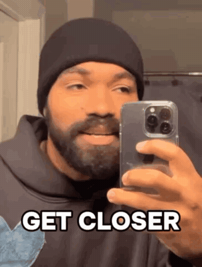 A Man With A Beard Is Taking A Selfie In Front Of A Mirror With His Phone . GIF
