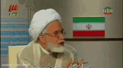 A Man With A Beard Is Talking In Front Of A Refrigerator GIF