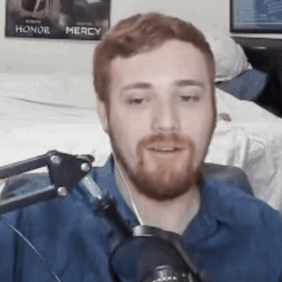 A Man With A Beard Is Talking Into A Microphone In A Room . GIF