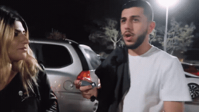 A Man With A Beard Is Talking To A Woman With A Skull On Her Jacket GIF