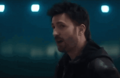 A Man With A Beard Is Talking To Another Man In A Dark Room . GIF